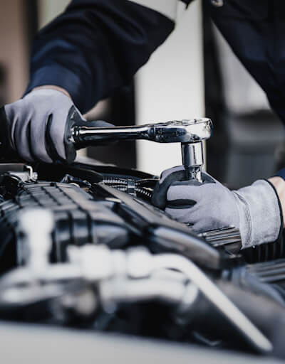 Mechanic leaning over a car engine, tightening a nut.