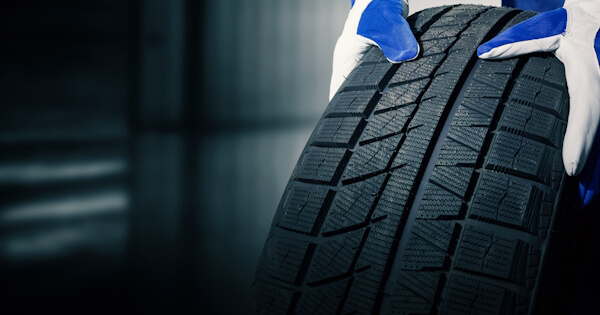 Close up of vehicle tire tread, with arms reaching into frame to carry tire.